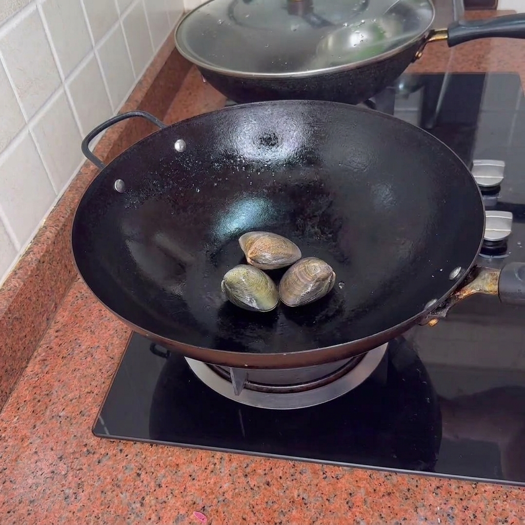 Tre vongole chiuse in un wok nero su un fornello.