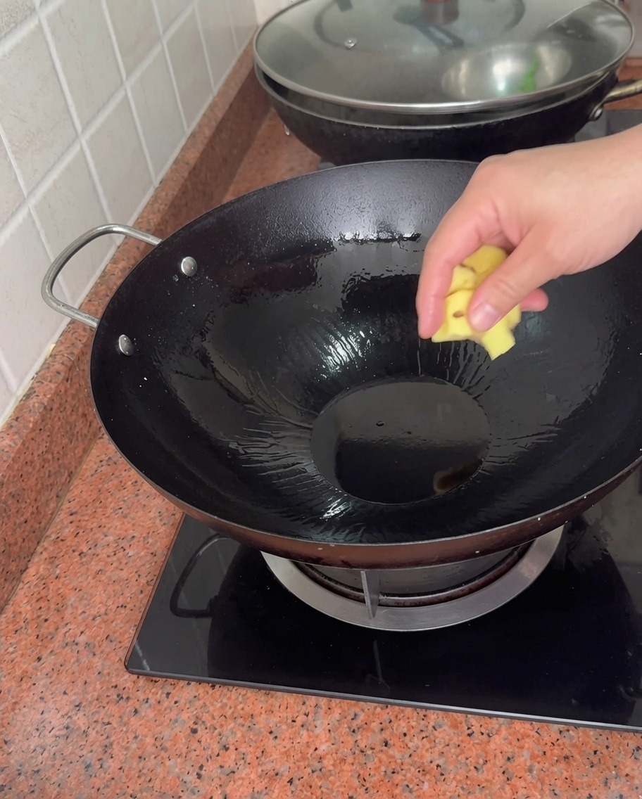 Una mano che lascia cadere un pezzo di zenzero in un wok caldo con olio.