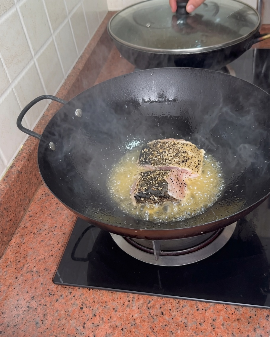 Pezzi spessi di cernia condita che rosolano nellolio bollente in un wok.