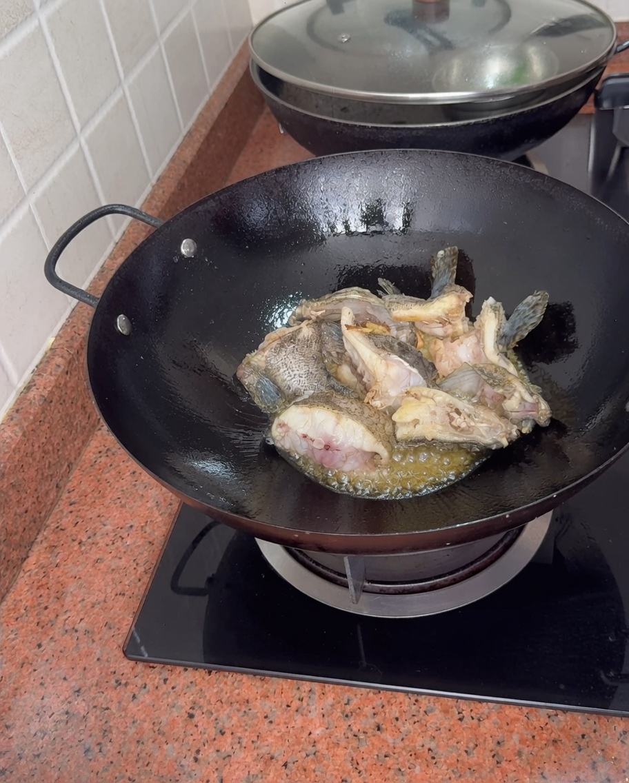 Pezzi di cernia che sobbollono in un wok mentre viene aggiunta acqua bollente, creando un denso brodo di pesce bianco.