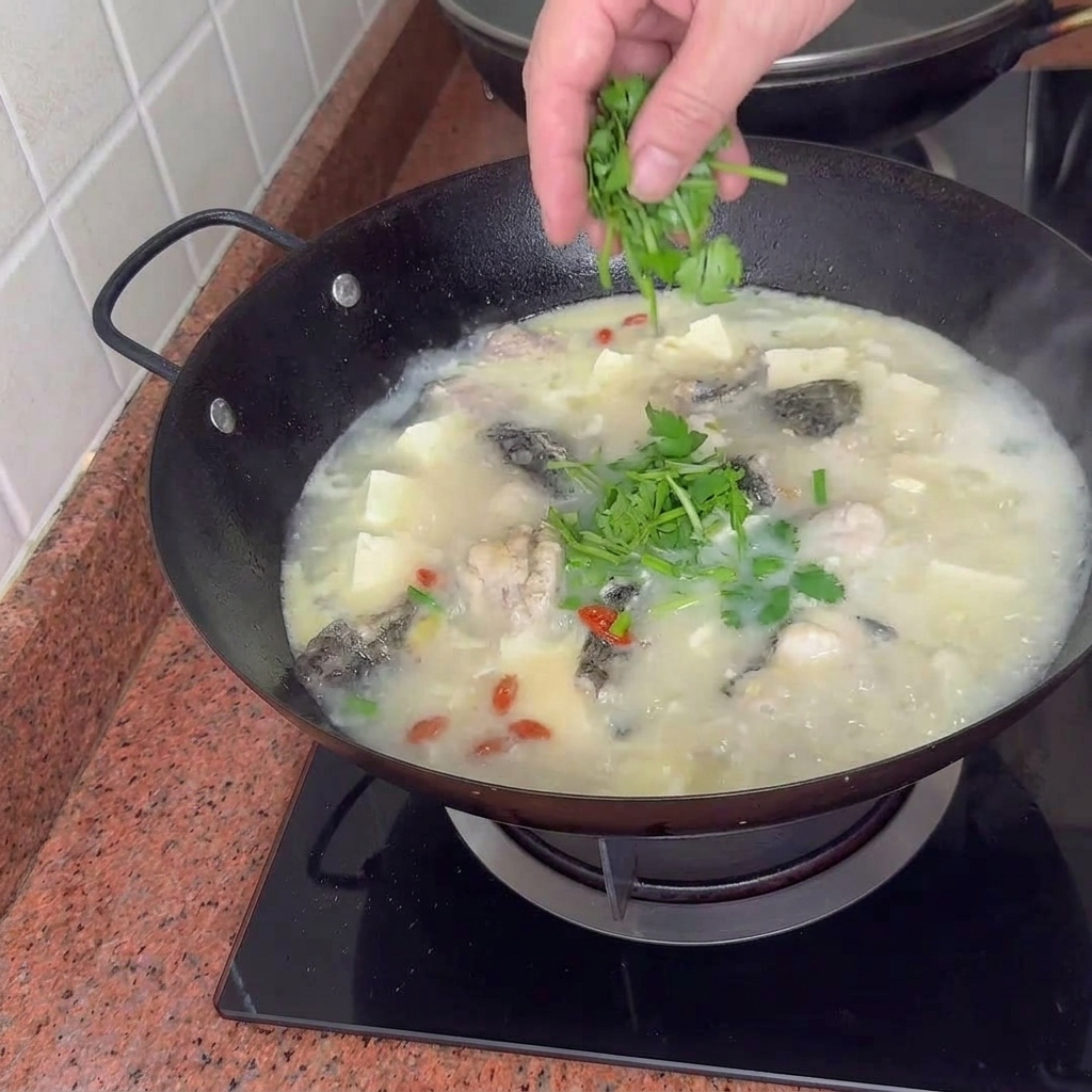 Una pentola finita di zuppa cremosa di pesce, tofu e vongole guarnita con cipollotti verdi vibranti.