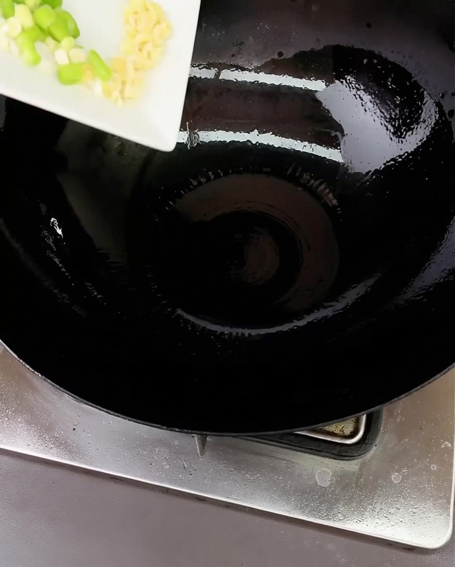 Cipollotti tritati e aglio sfrigolanti in un wok caldo con un filo dolio.