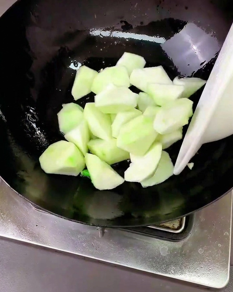 Pezzi di luffa saltati in un wok con gli aromatici.