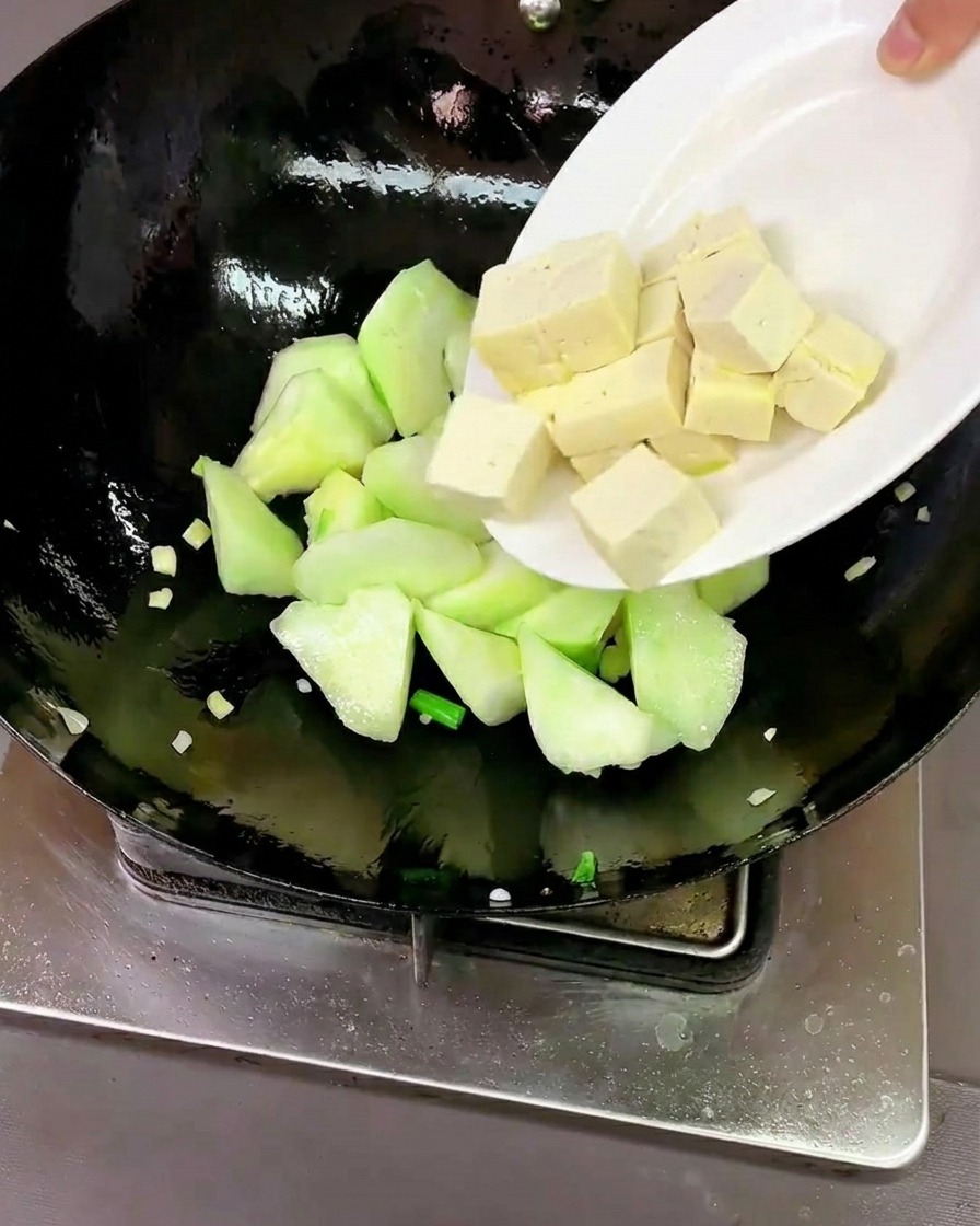 Cubetti di tofu fresco e vongole crude pulite aggiunti nel wok con la luffa.