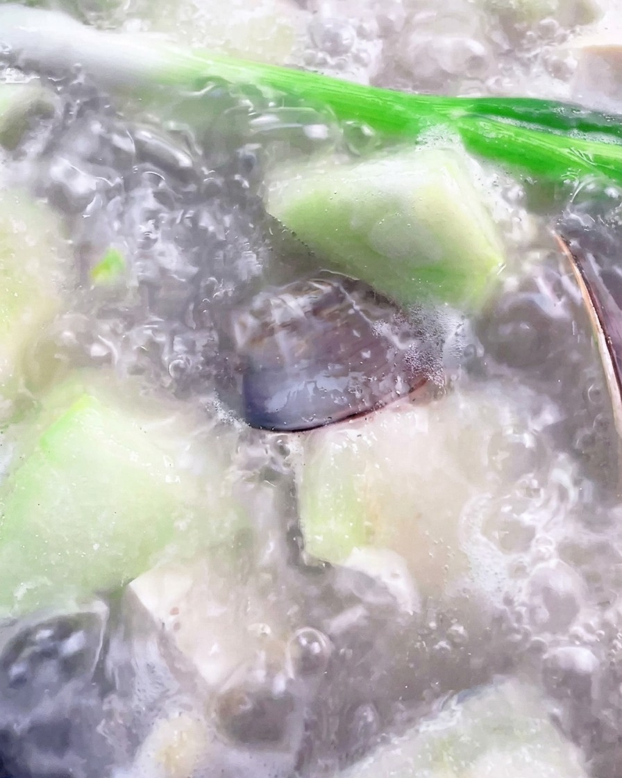Un mestolo che rimuove la schiuma bianca dalla superficie della zuppa di luffa e vongole che bolle in pentola.