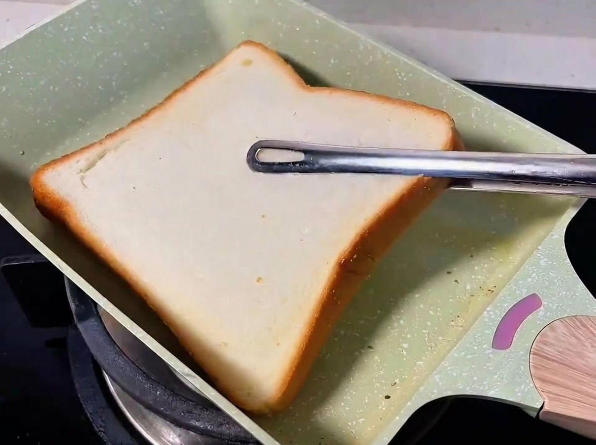 Una fetta di pane bianco che tosta in una padella verde.