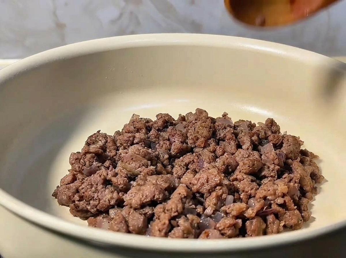 Macinato di manzo che viene mescolato e sgranato in padella con la cipolla.