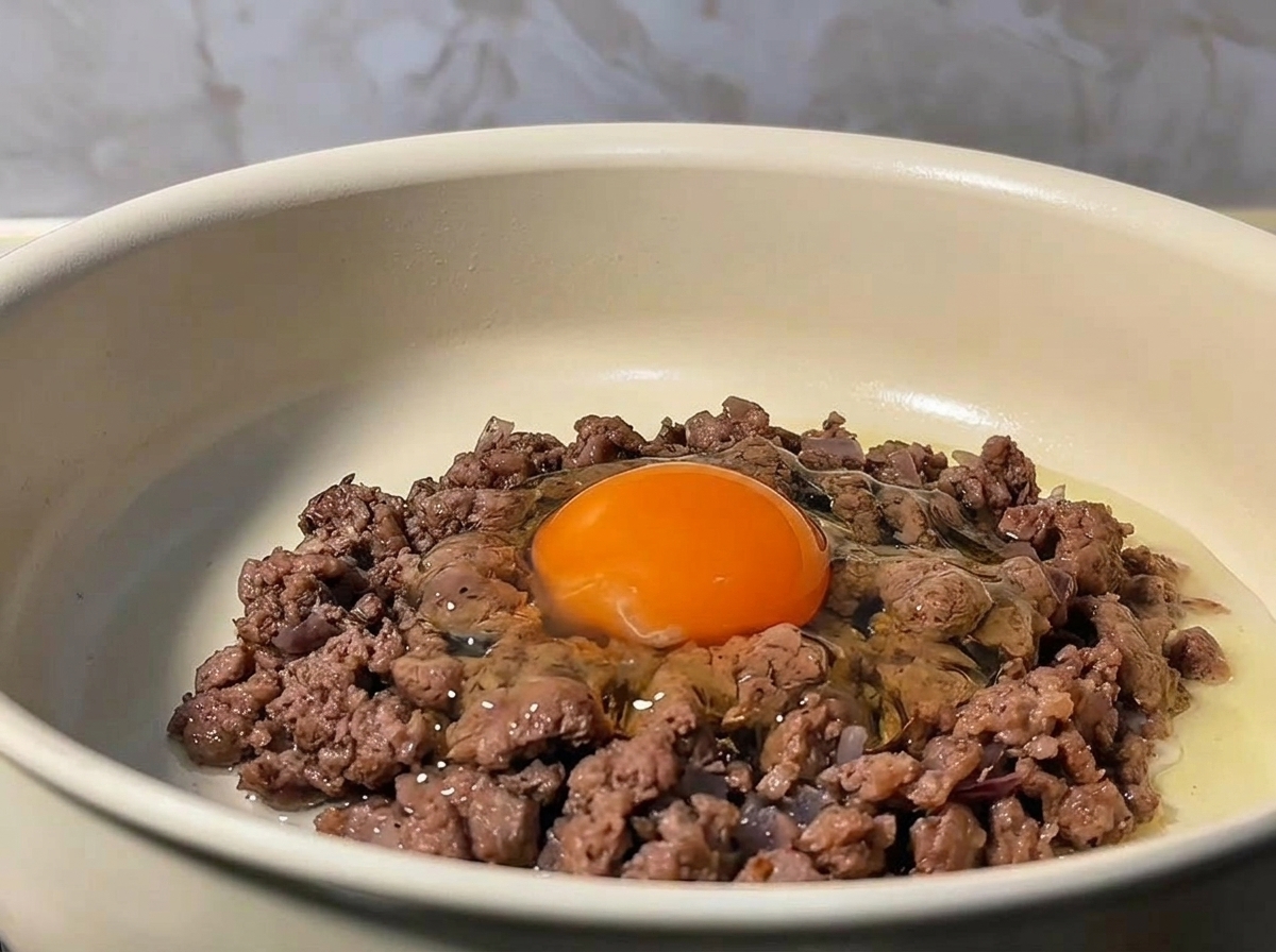 Un uovo crudo rotto al centro del macinato di manzo rosolato in padella.