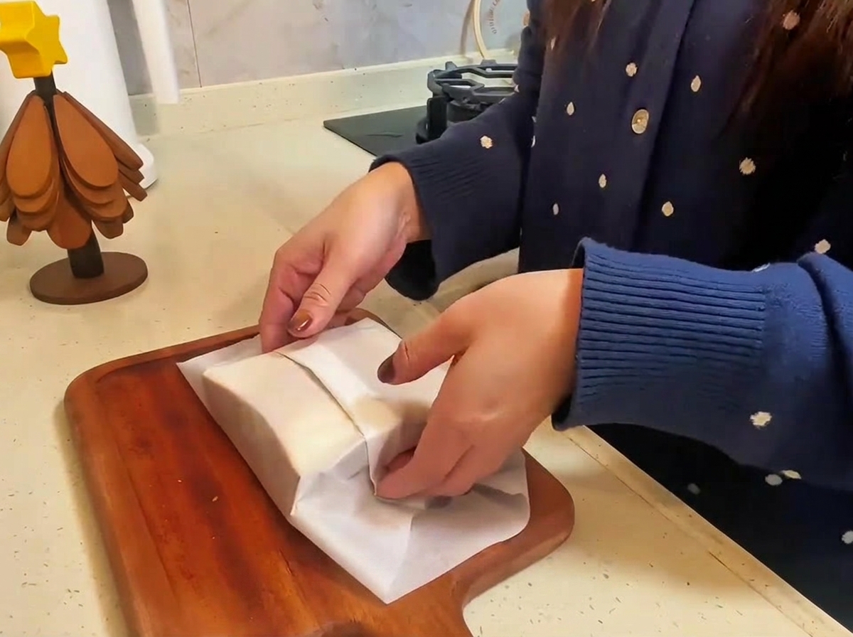Il panino finito con manzo e formaggio avvolto in carta forno mentre viene tagliato a metà su un tagliere di legno.