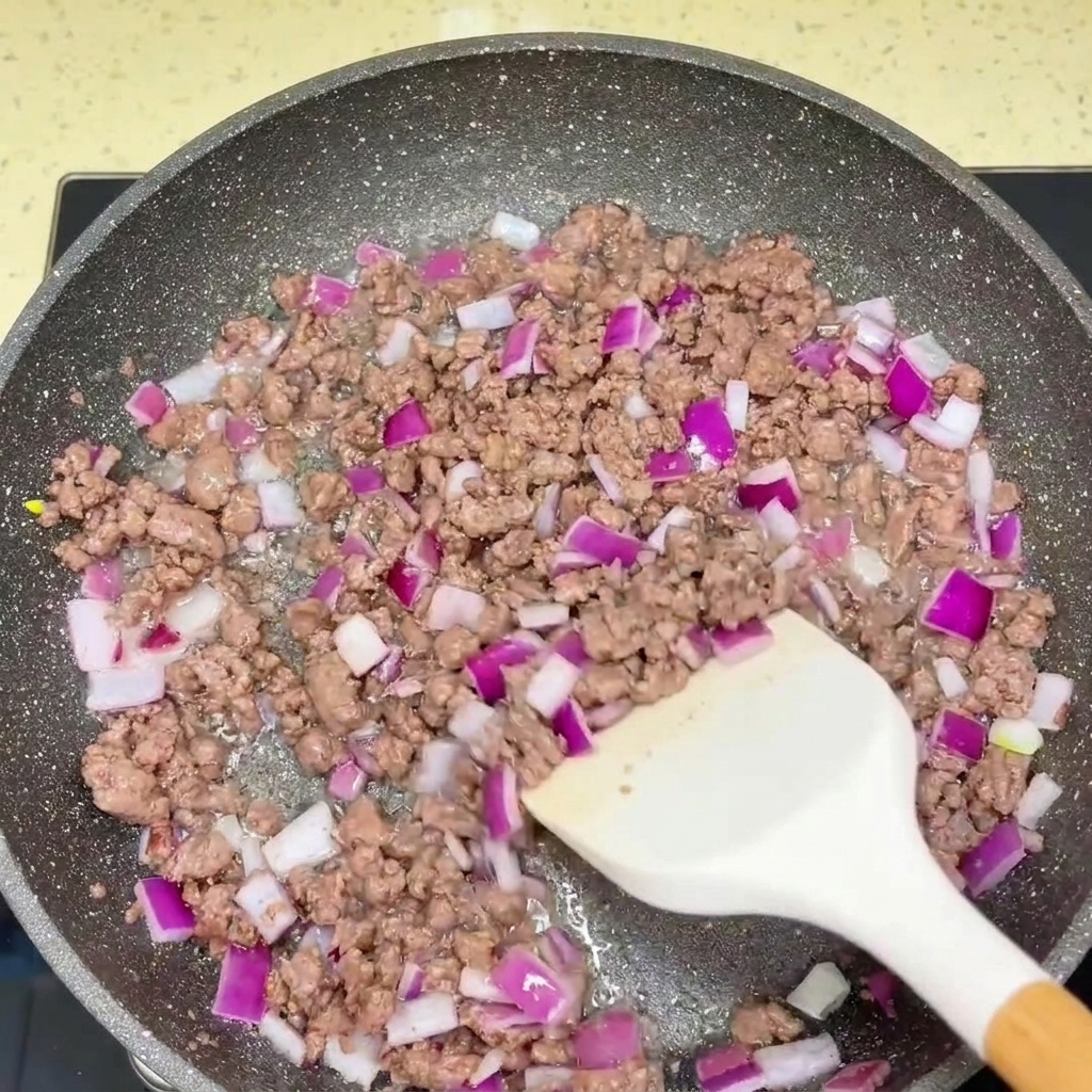 Manzo macinato saltato e cipolla rossa tritata che vengono conditi con salse in una padella.