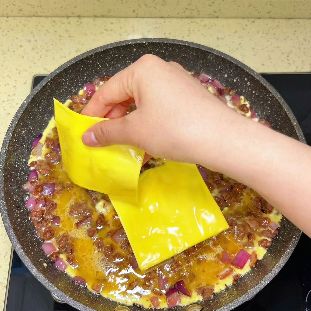 Fette di formaggio fuso adagiate sopra le uova e il manzo in una padella.