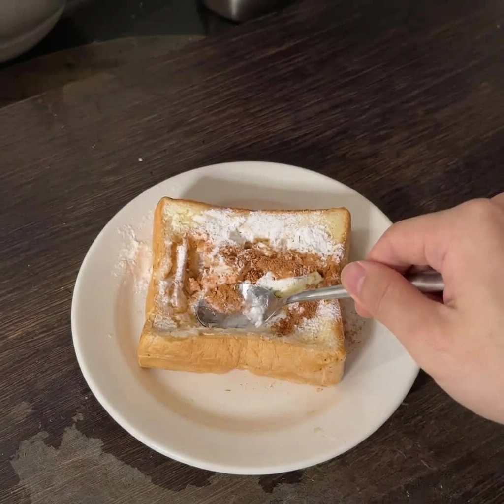 Una mano che usa un cucchiaio di metallo per premere al centro di una spessa fetta di pane bianco su un piatto bianco.