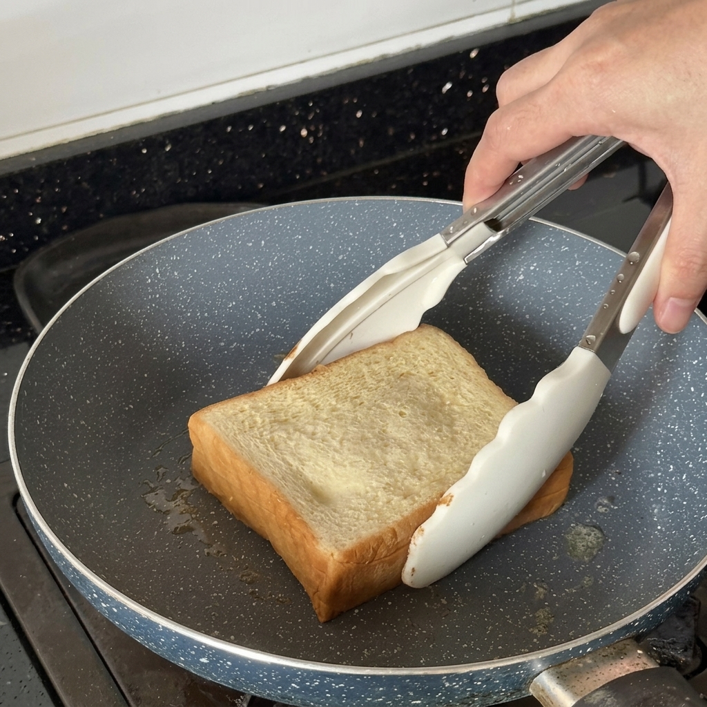 Una spessa fetta di pane tostata in una padella usando pinze bianche.