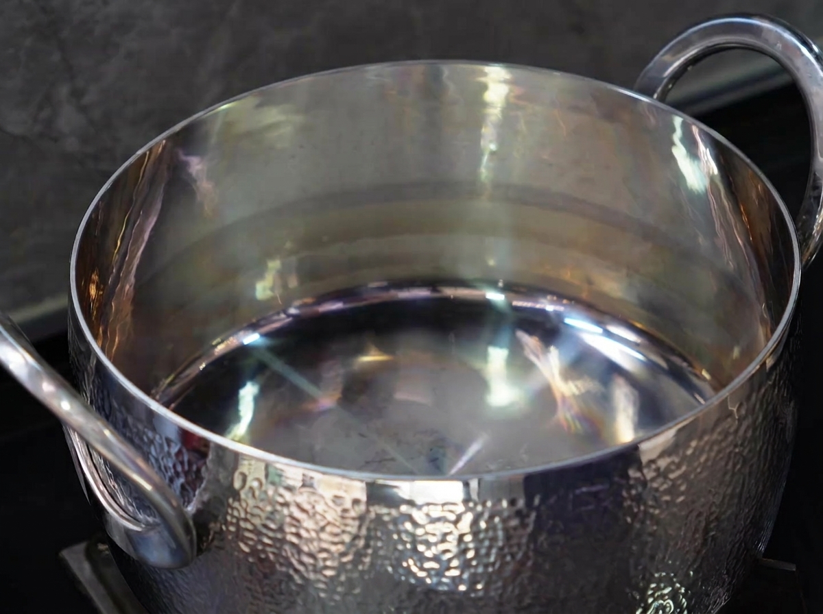 Un primo piano di un cucchiaio di olio da cucina versato in una pentola in acciaio inossidabile vuota e lucida.