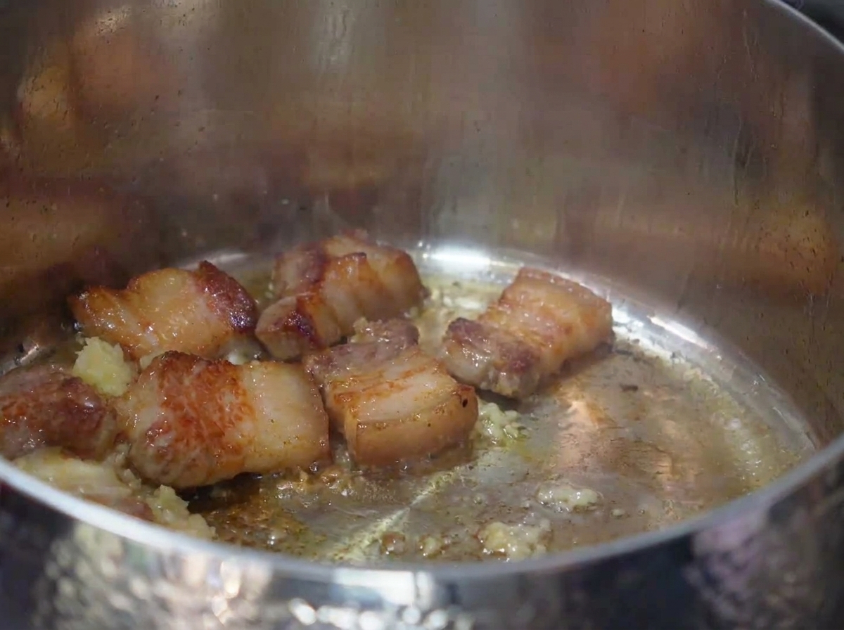 Kimchi tritato mescolato nella pentola con la pancetta rosolata e laglio.