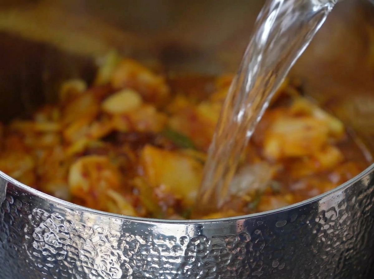 Acqua versata nella pentola con la miscela di kimchi e pancetta.