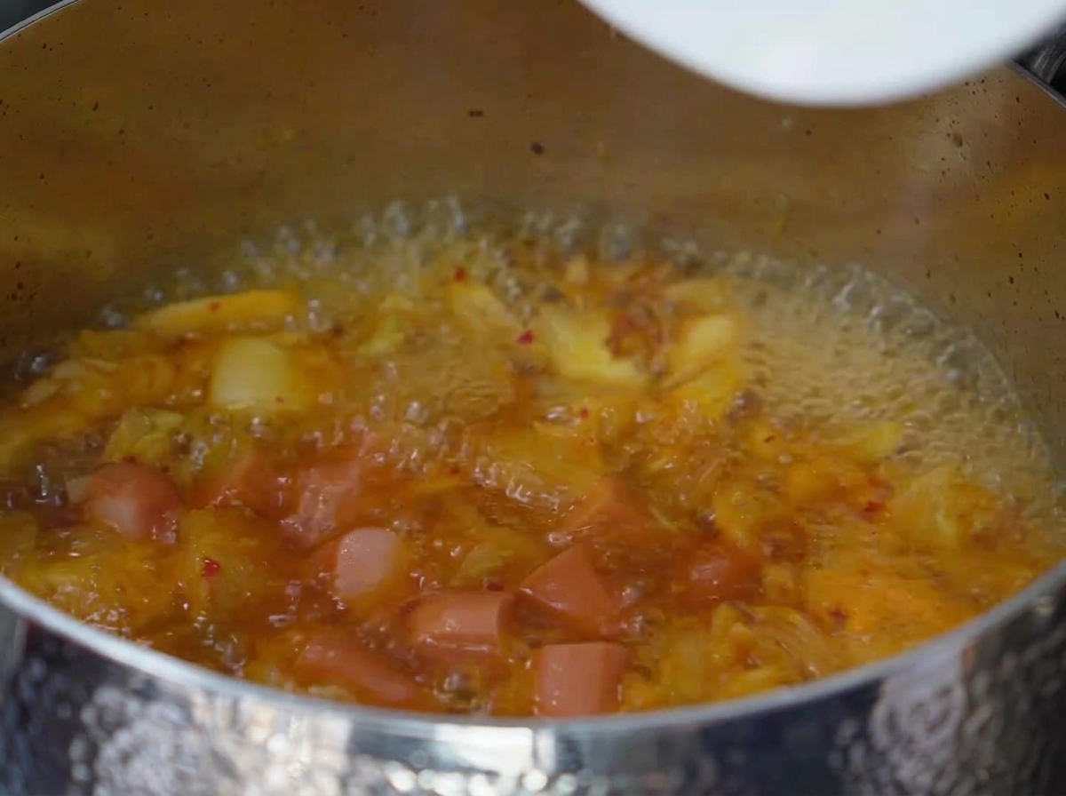 Fette di spam e salsiccia che sobbollono nel brodo di kimchi bollente e condito.
