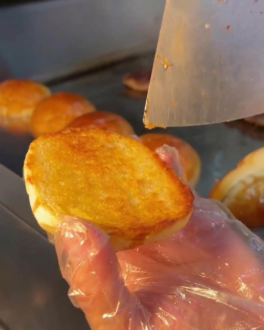 Un cucchiaio di metallo che spalma una salsa bianca cremosa sulla superficie tostata di un panino.
