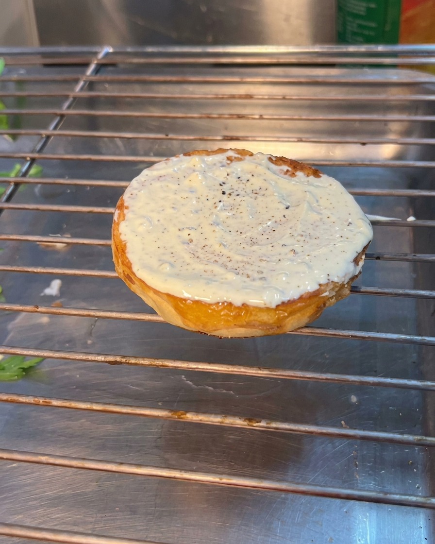 Lassemblaggio del burger che mostra rucola, pomodoro e cetriolini posizionati sul pane tostato inferiore.