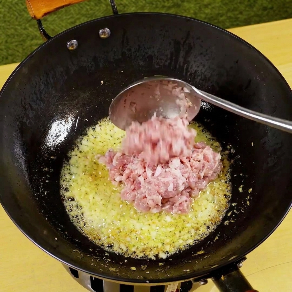 Carne di maiale tritata aggiunta in padella con cipolla e aglio soffritti, che inizia a rosolare.