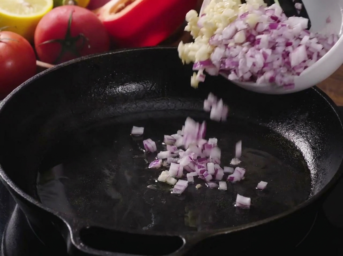 Cipolle a cubetti e aglio tritato versati in una padella di ghisa calda e oliata.