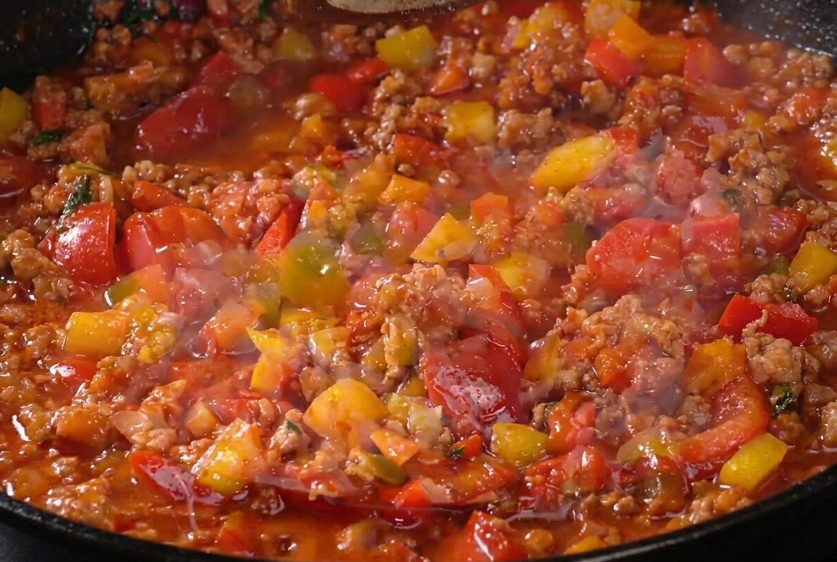 Il ragù di carne sobbolle in padella mentre viene condito con pepe, mostrando una consistenza ricca e densa.
