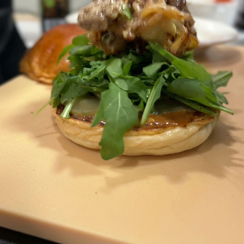 Uno spesso strato di manzo e cipolle rosse saltati, sormontato da formaggio fuso, adagiato su un letto di rucola fresca.