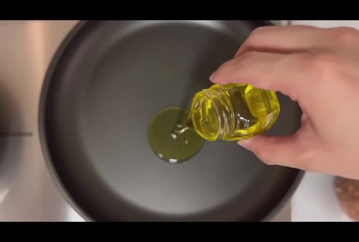 Quattro polpette in padella con olio e spicchi daglio.
