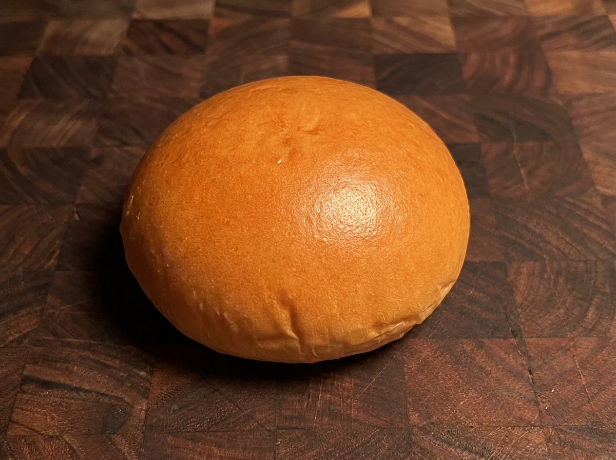 Un panino per hamburger tostato dorato su una superficie di legno.
