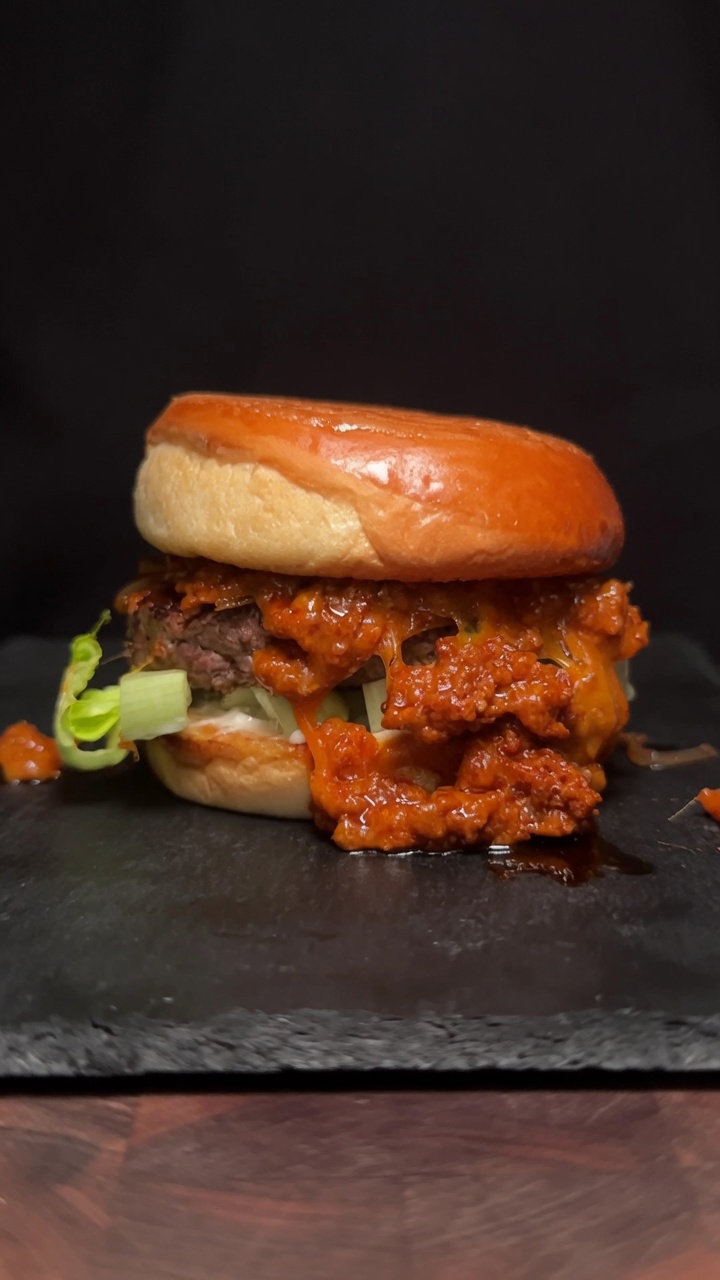 Un gourmet Burger al Choriqueso con un hamburger di manzo spesso e una vibrante salsa al formaggio e chorizo su un panino tostato.