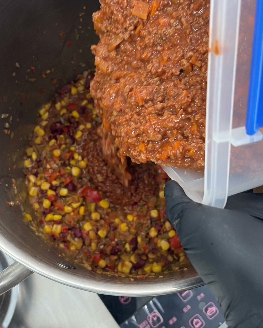 Un ricco ragù di carne versato in una grande pentola piena di verdure e spezie.