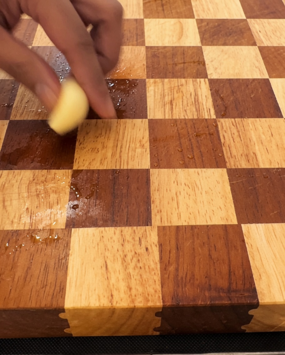 Spicchi daglio tritati finemente su un tagliere di legno con un grosso coltello.