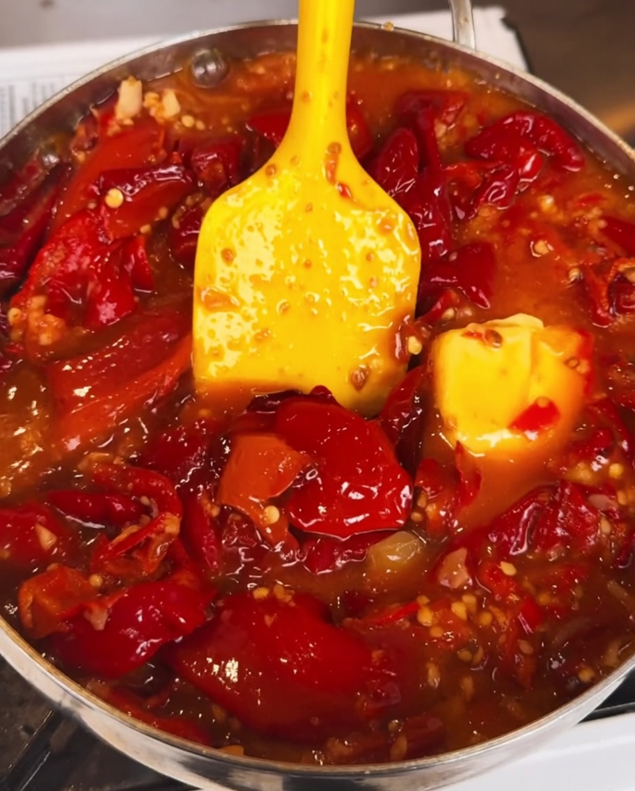 La salsa al peperoncino che sobbolle in una padella mentre viene mescolata una salsa densa e scura, creando una finitura ricca e lucida.