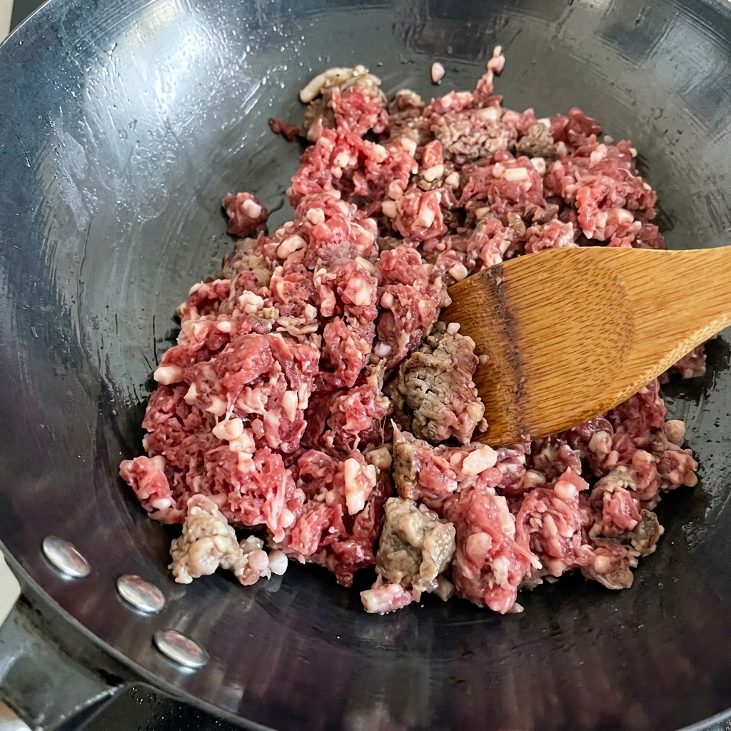 Manzo fresco macinato saltato in un wok caldo, che cambia colore da rosso a marrone.