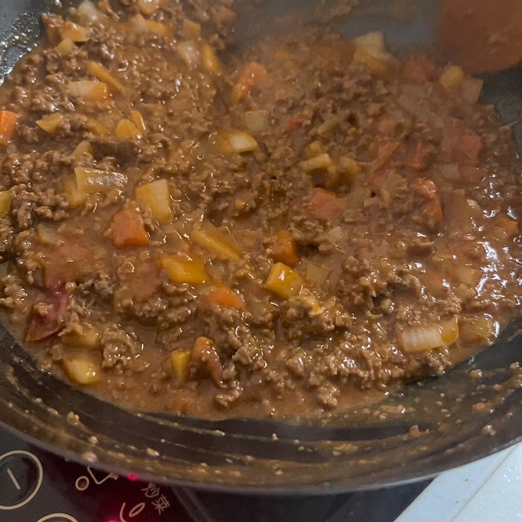 Una salsa ricca e scura mescolata al composto di carne e verdure in un wok caldo.