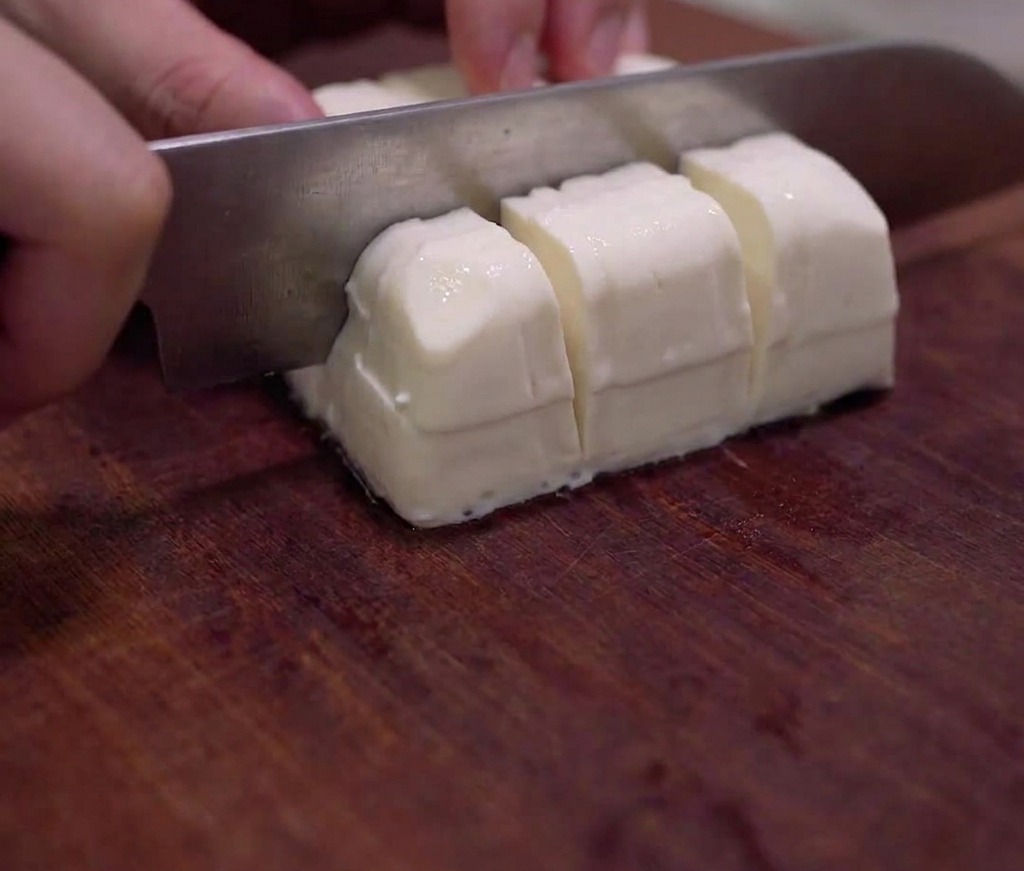 Un blocco di tofu morbido tagliato con cura a cubetti su un tagliere di legno.