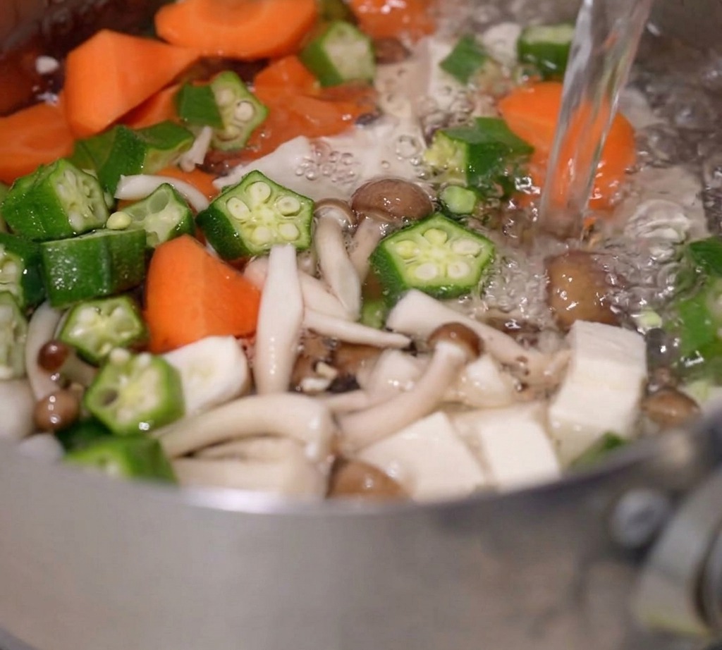 Acqua bollente versata in una pentola contenente verdure e tofu.