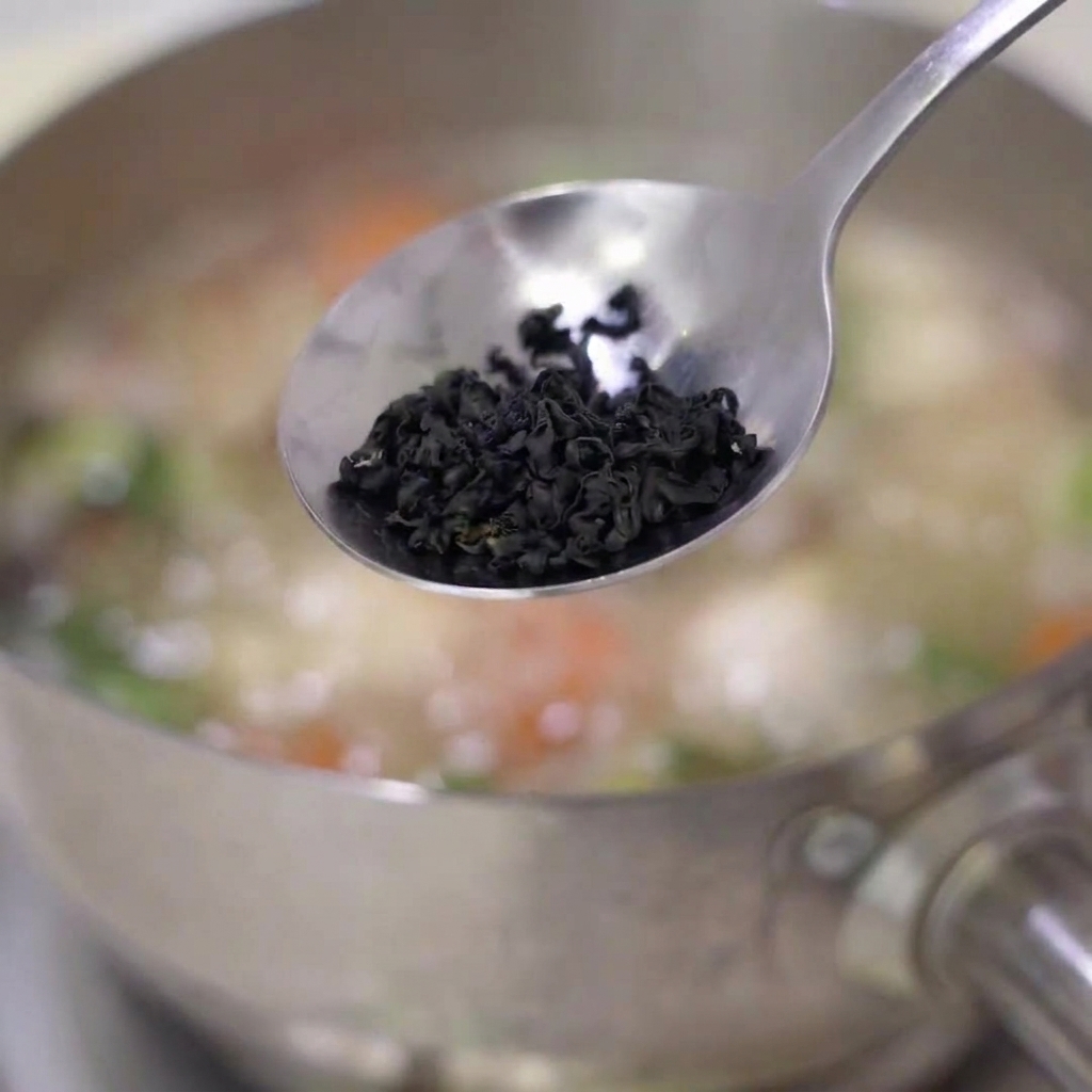 Alga wakame secca aggiunta in una pentola di zuppa in ebollizione.