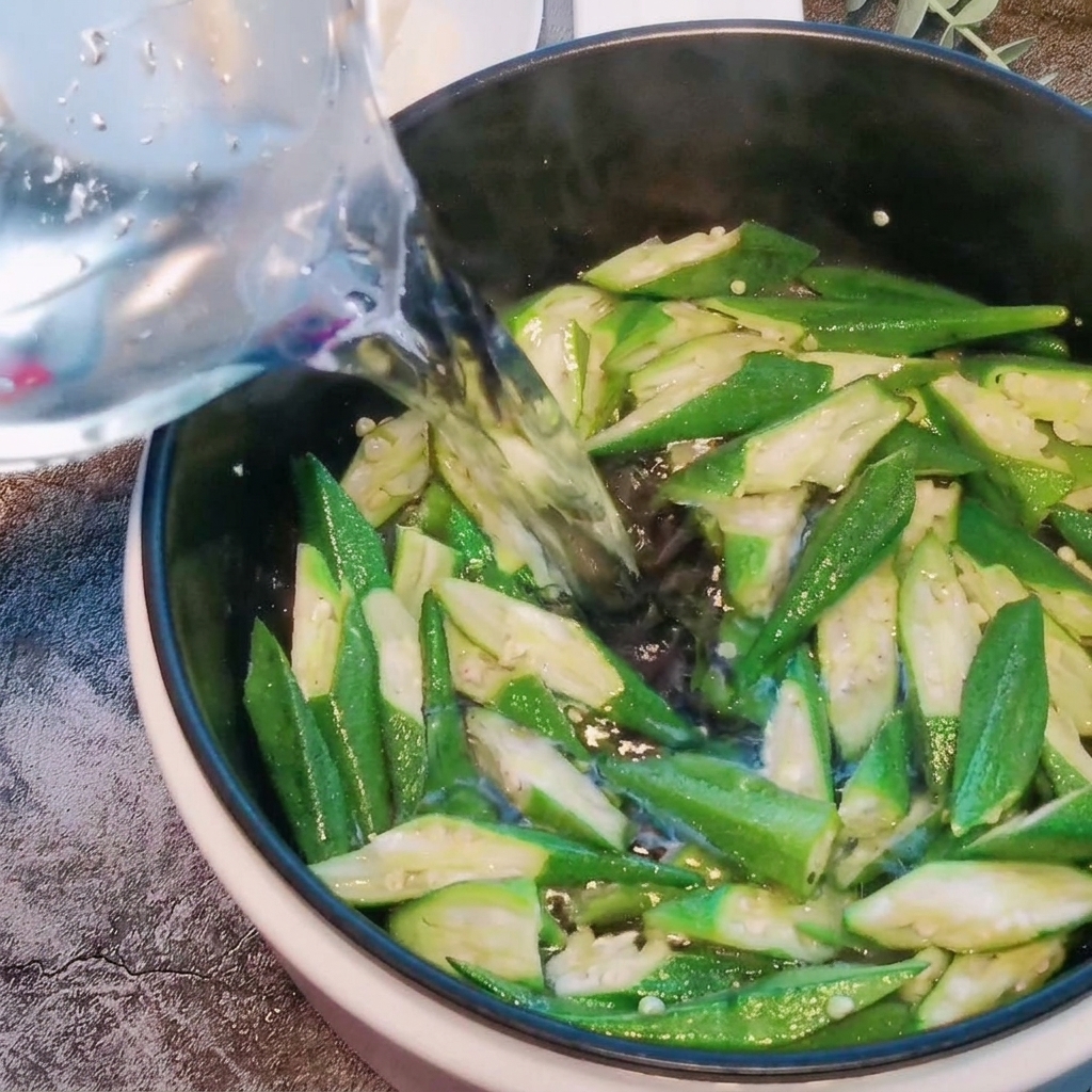 Acqua versata in una pentola contenente i pezzi di okra saltati.