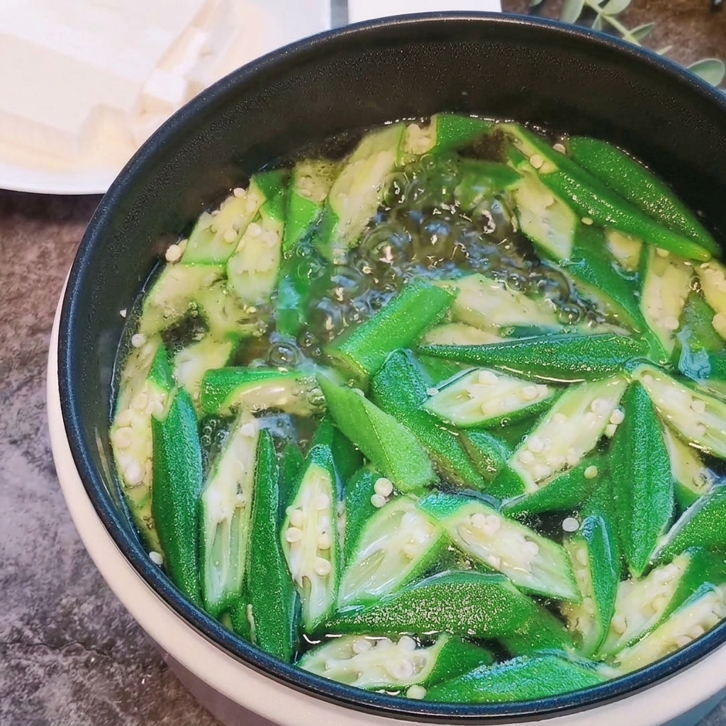 Cubetti di tofu morbido aggiunti a una pentola bollente di okra e acqua.