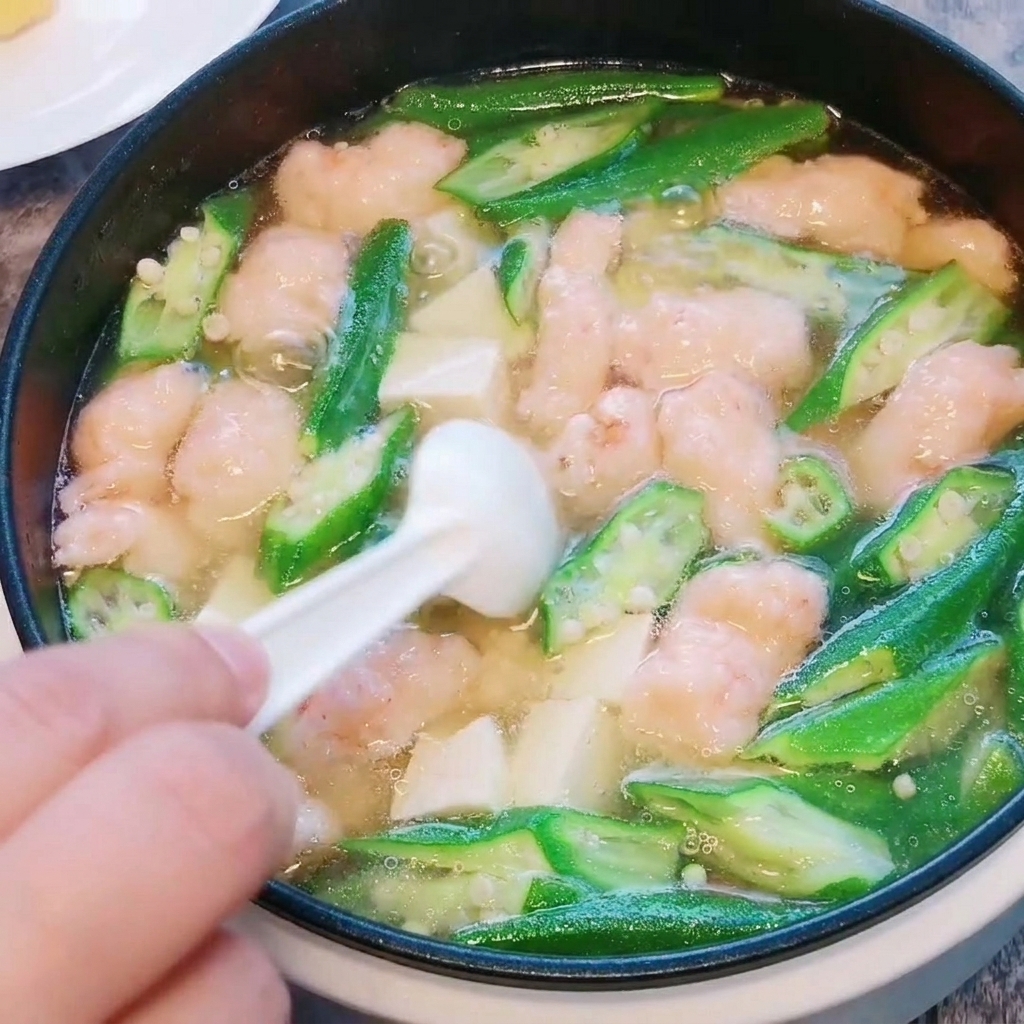 Primo piano di sale e pepe bianco sparsi nella zuppa finita di okra, tofu e pasta di gamberi.