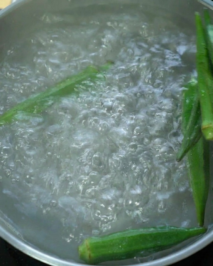 Baccelli di okra verde fresca che bollono in una pentola dacqua.