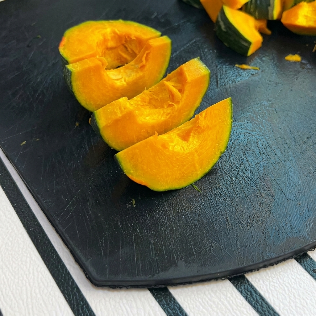 Piccoli spicchi di zucca verde su un tagliere nero.