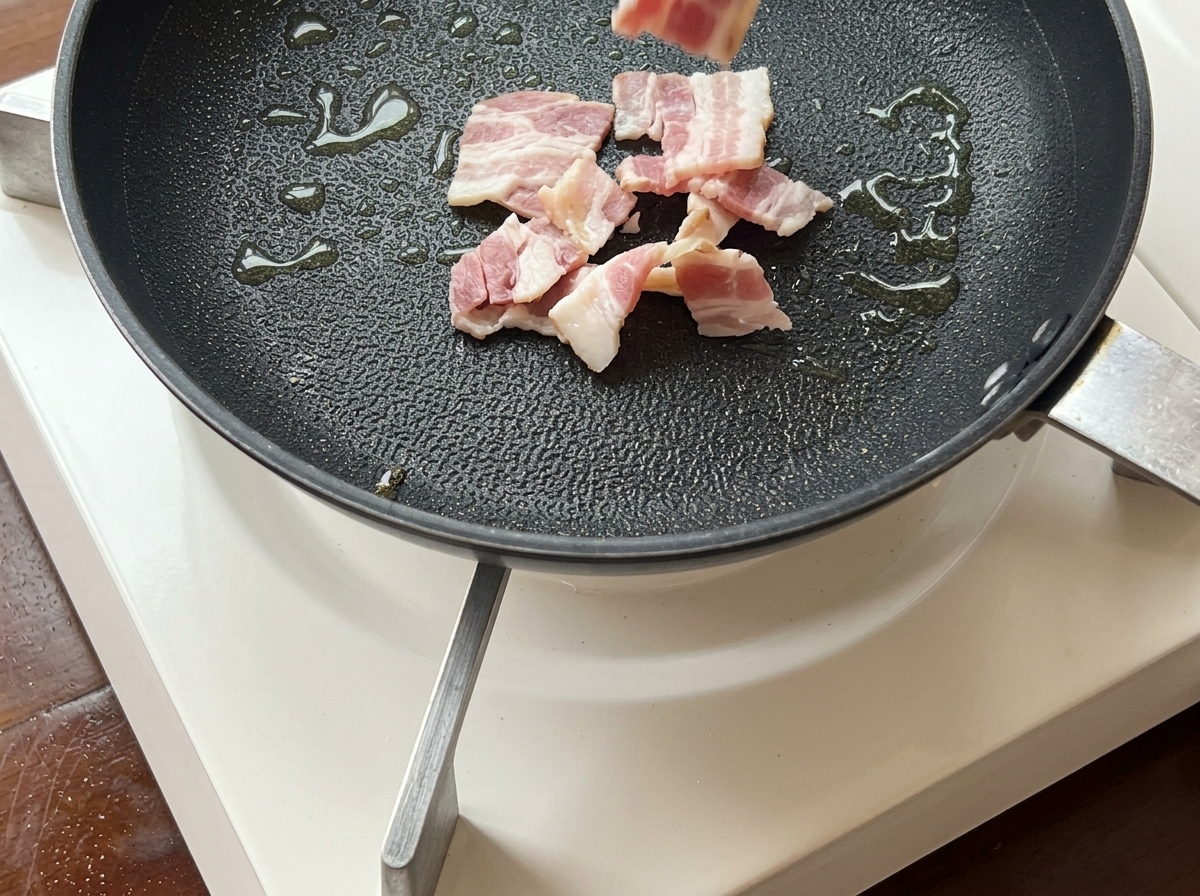 Strisce di bacon che sfrigolano in padella fino a diventare dorate e croccanti.