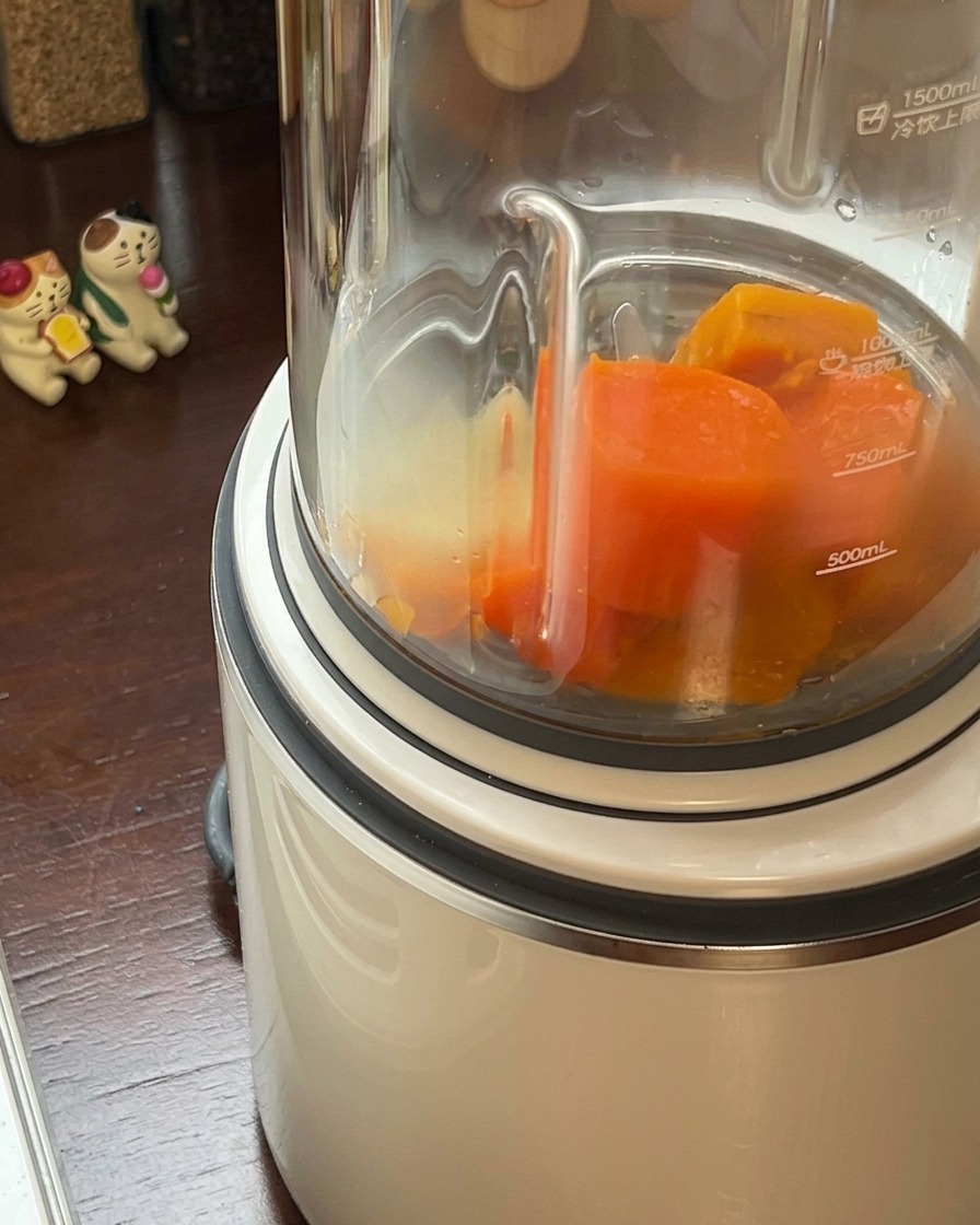 Il composto di zucca e carote cotte che viene versato nel bicchiere di un frullatore ad alta potenza.