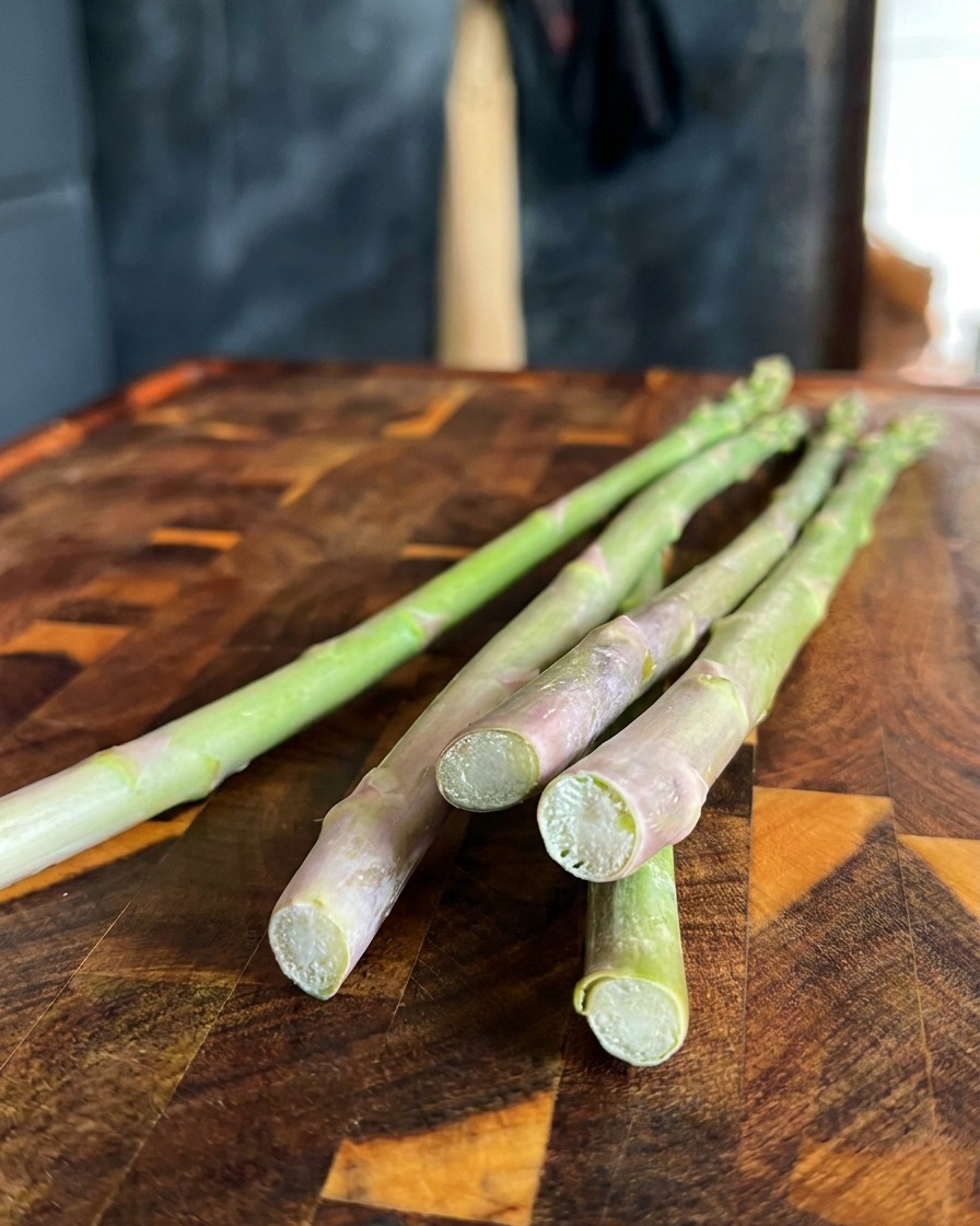 Primo piano di asparagi verdi freschi mentre si tagliano le estremità dure su un tagliere di legno.