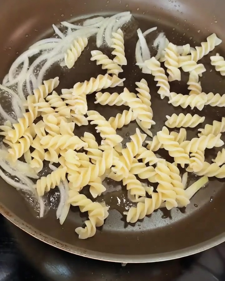 Pasta a spirale cotta aggiunta in una padella con le cipolle soffritte.