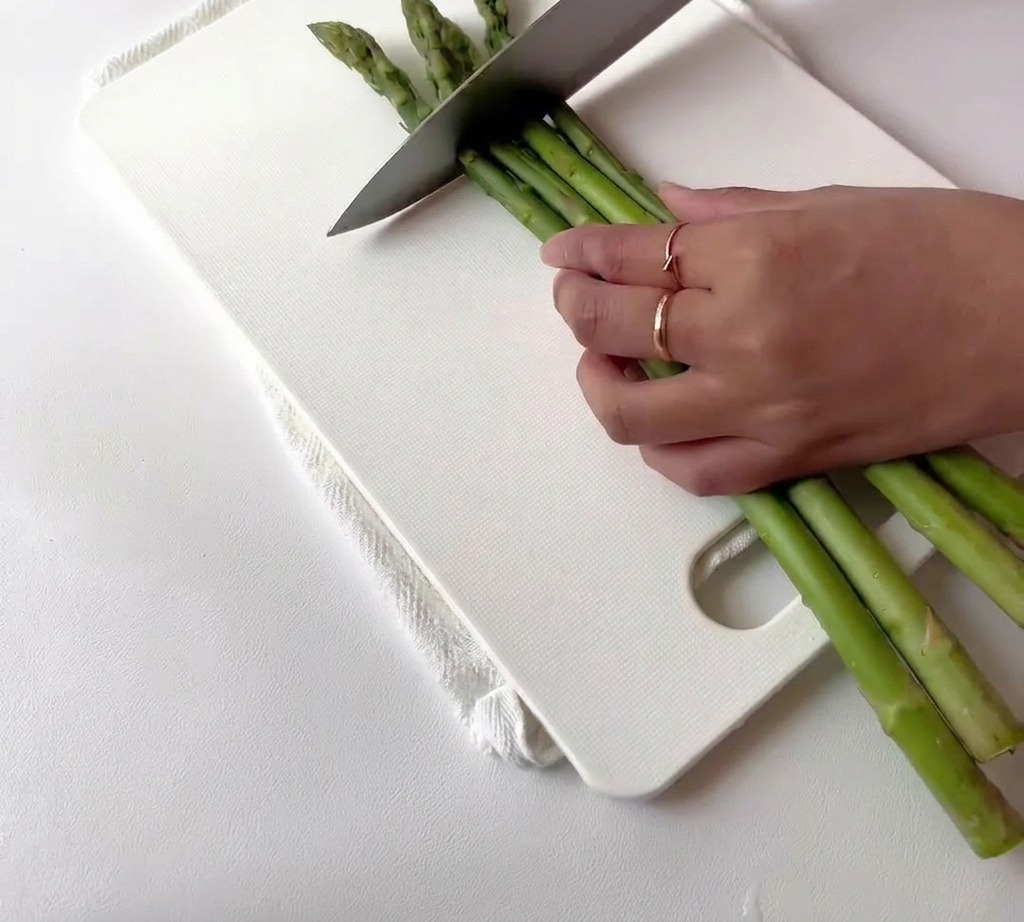 Asparagi verdi freschi tagliati a pezzetti su un tagliere bianco.