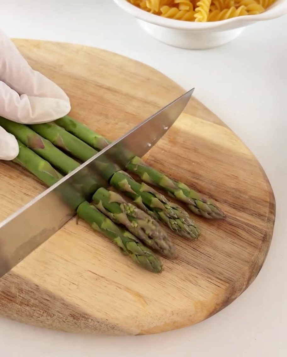 Asparagi verdi freschi tagliati a pezzetti su un tagliere di legno.
