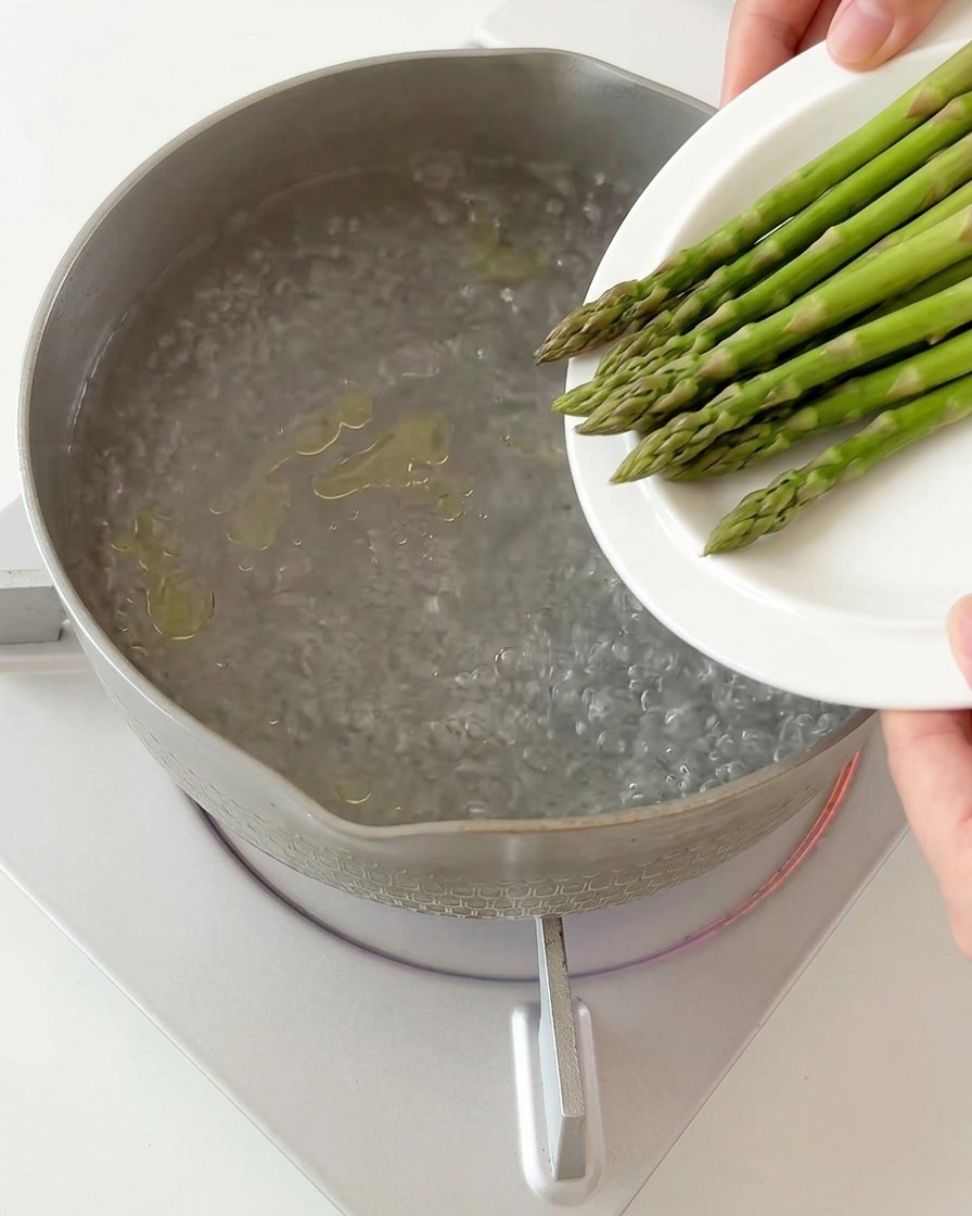 Pezzetti di asparagi versati nella pentola con la pasta in ebollizione.
